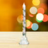 Tall, slim advent candle. Candle is white and is decorated with sprigs of holly and red berries. The numbers 1 to 24 run down the candle from top to bottom.
