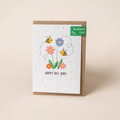 Plantable card with illustration of two bees buzzing around colourful flowers. Text below the image reads Happy Bee Day.