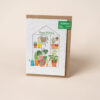 A plantable birthday card with an illustration of a greenhouse which contains colourful pots, plants and flowers. Text on the front reads Happy Birthday.