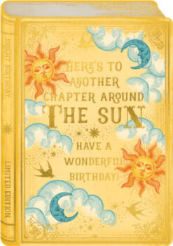 Birthday card in the shape of a book. Bright yellow coloured card decorated with suns and moons. Text reads Here's to Another Chapter Around the Sun - Have a Wonderful Birthday.