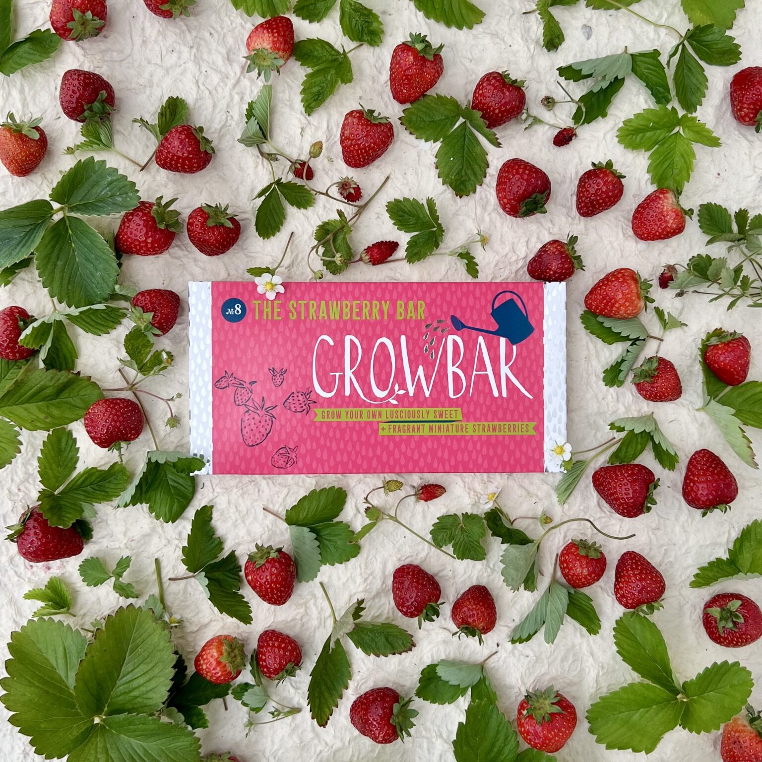 A pink plantable strawberry growbar sits in amongst strawberries and leaves.