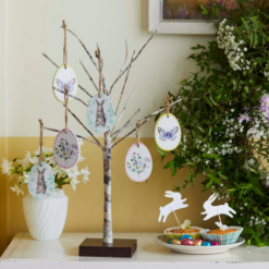 A small stick tree is decorated with easter hanging decorations which have images of bunnies, butterflies and flowers on them.