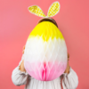 A child holds a large ombre easter egg infront of their face. The egg is yellow white and pink.
