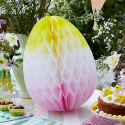 A large white, yellow and pink ombre honeycomb egg sits on a table decorated with Easter treats.