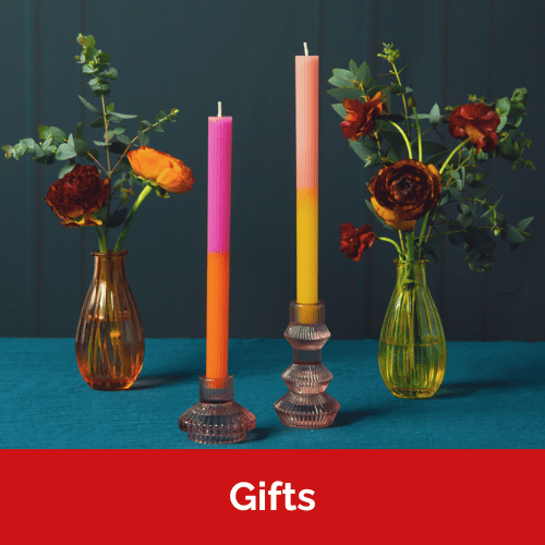 Two ombre dinner candles in holders with a vase of flowers either side. The candles are pink and orange, and pink and yellow.