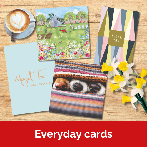 A selection of greetings cards on a wooden table next to a coffee and a bunch of daffodils.