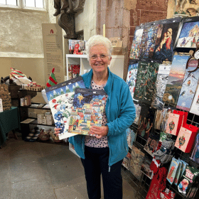 A lady holds two advent calendars whilst standing in front of a display of more advent calendars in a Cards for Good Causes pop up Christmas shop.