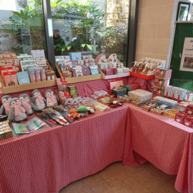 Tables covered with red and white gingham table cloths are displaying a range of gifts in a Cards for Good Causes Christmas shop.
