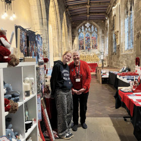 Two ladies stand in a Cards for Good Causes pop up Christmas shop in a church.