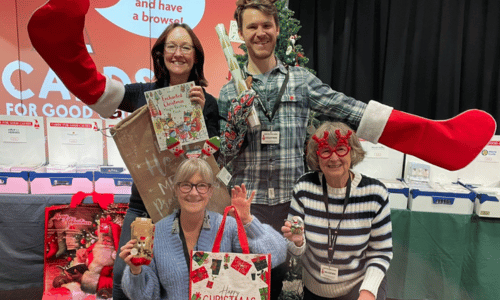 Four people wearing Christmas accessories and holding Christmas gifts in the Christmas shop at The Forum, Norwich.
