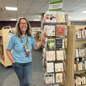 A lady stands beside a card spinner in Blackheath Library.