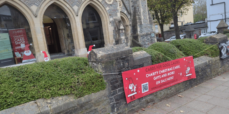 Photograph of the outside of Tyndale Baptist Church in Bristol. A red Cards for Good Causes banner hangs on the railings outside.