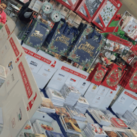 Display of charity Christmas card boxes and Christmas gift bags hanging up at the back.