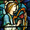 Christmas card with a stained glass image of an angel with turquoise wings playing a harp