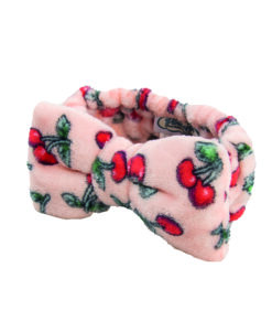 A soft fleece head band with a bow on the top. The band is pink with a red and green cherry pattern.
