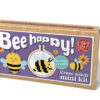 Cross stitch mini kit box featuring a cheerful bee design in a small embroidery hoop, with purple label, floral illustrations, and playful text reading “Bee happy!” and “Keyring included.”