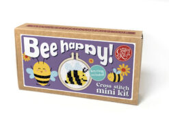 Cross stitch mini kit box featuring a cheerful bee design in a small embroidery hoop, with purple label, floral illustrations, and playful text reading “Bee happy!” and “Keyring included.”