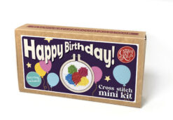 Cross stitch mini kit box featuring a colourful balloon design in a small embroidery hoop, with bright packaging and large white text reading “Happy Birthday!” Includes note that a keyring is included.
