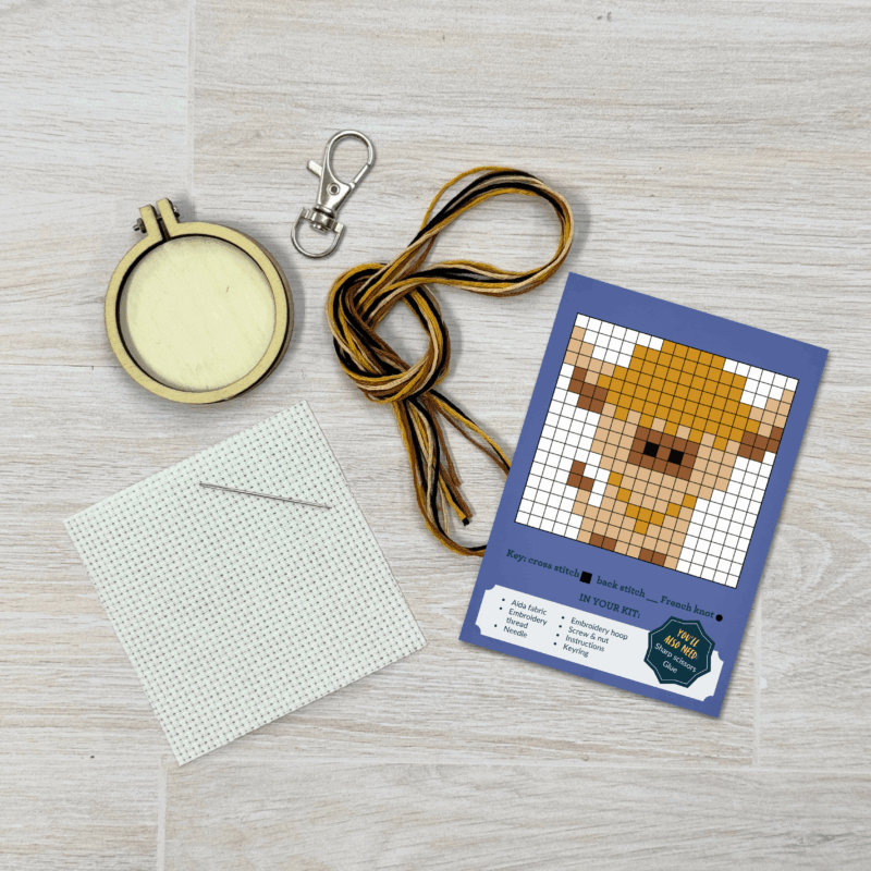 Contents of this product including embroidery hoop, keyring, fabric, needle, thread, and Highland Cow pattern