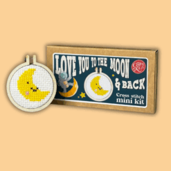 Cross stitch mini kit box featuring a crescent moon with a smiling face in a mini embroidery hoop. A small astronaut is featured on the box. Includes playful text “Love you to the moon & back” and “Keyring included.”