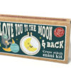 Cross stitch mini kit box featuring a crescent moon with a smiling face shown in a tiny embroidery hoop. A small astronaut is featured on the box. Includes playful text “Love you to the moon & back” and “Keyring included.”
