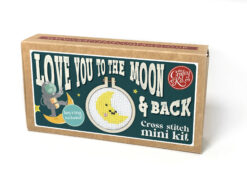 Cross stitch mini kit box featuring a crescent moon with a smiling face shown in a tiny embroidery hoop. A small astronaut is featured on the box. Includes playful text “Love you to the moon & back” and “Keyring included.”