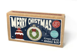 Cross stitch mini kit box with bold “Merry Christmas” text, festive wreath design in a small embroidery hoop, and cartoon chimney with an upside down Santa who's legs are sticking out.