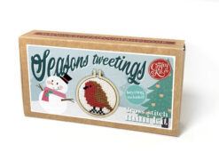 Cross stitch mini kit box featuring a festive robin design in a small embroidery hoop, with snowman, Christmas tree, and snowflake background. Text reads “Seasons tweetings” and “Keyring included.”