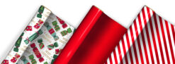 Three rolls of Christmas wrapping paper displayed side by side—one with colourful festive Christmas crackers and gold ‘MERRY CHRISTMAS’ text, one solid metalic red, and one with red and white diagonal candy cane stripes.