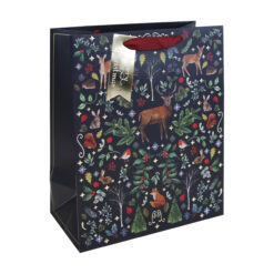 A navy Christmas gift bag with woodland pattern featuring trees, foliage and woodland animals. The bag has red handles and a gold tag.