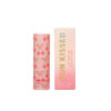 A pink lip balm stick with red cherry pattern next to the box.