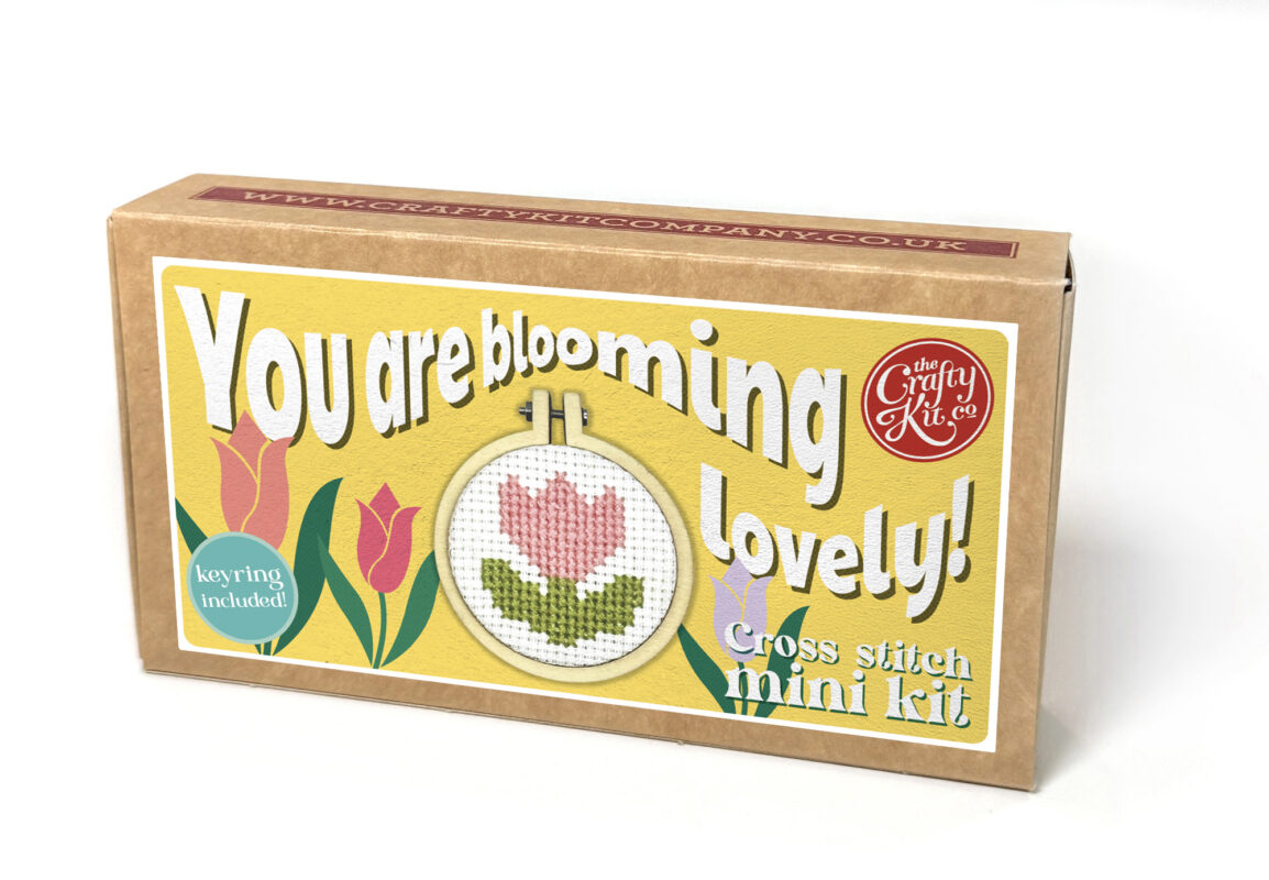 Cross stitch mini kit box featuring a pink tulip design in a small embroidery hoop, with playful yellow label and text reading “You are blooming lovely” and “Keyring included.”