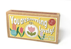 Cross stitch mini kit box featuring a pink tulip design in a small embroidery hoop, with playful yellow label and text reading “You are blooming lovely” and “Keyring included.”