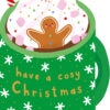 Christmas card featuring a green mug of hot chocolate topped with whipped cream, pink marshmallows, colourful sprinkles, and a smiling gingerbread man. The mug reads 'have a cosy Christmas' in cheerful yellow and orange lettering.