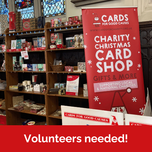 An image of a Cards for Good Causes pop-up shop with red banner, charity Christmas cards and gifts. Text reads 'Volunteers needed!'.