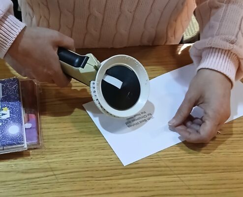 Hands hold a braille labelling machine. The printed braille greeting is being placed inside a Christmas card.