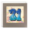 Square card with grey border. Illustration of the number 21 in a blue graffiti style. Behind the number is a clear square window which contains colourful paper confetti.
