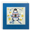 A square card with blue border and translucent centre through which you can see paper confetti stars and dots. Illustration on the front of the card of a penguin on skis, along with the text 'Merry Crimbo'.