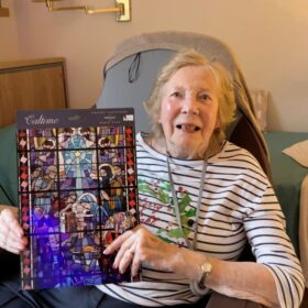 A lady in a striped jumper smiles at the camera as she hols up a Religious Advent Calendar.