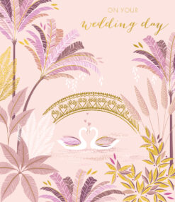 A pale pink card with an illustration of two swans on a lake surround by palm treets and lush foliage. A delicate gold bridge across the lake and gold text reading 'On your Wedding Day'.