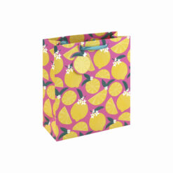 A medium pink gift bag decorated with lemons, lemon slices, green leaves, white flowers, and finished with ribbon handles and a lemon‑shaped tag.