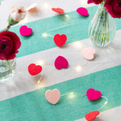 Red, pink and magenta felt heart string lights arranged on a striped surface with vases of flowers.
