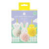 A brightly coloured craft kit package labelled ‘Easy Peasy Pom Pom Kit,’ showing three hanging pom‑pom characters - a white-pom sheep, a pink‑pom bunny and a yellow‑pom chick - against a spring scene with a picket fence, grass, flowers and clouds.