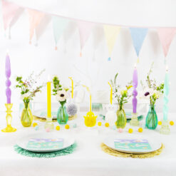 Pastel Easter table with candles, floral vases, bunny and chick napkins and showcasing the hanging pom‑pom ornaments.
