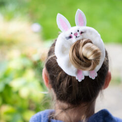 White fluffy bunny scrunchie with ears and embroidered face worn in a hair bun outdoors.