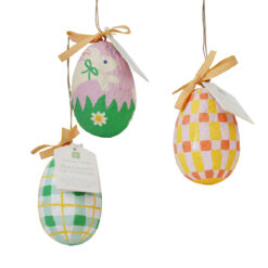 Three hanging Easter egg decorations made from patterned recycled fabric, one green check, one pink with a bunny design, and one orange check, each topped with a yellow‑striped bow and a tag.