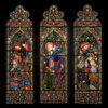 Three ornate stained glass windows depicting biblical scenes with angels, saints, and floral patterns.